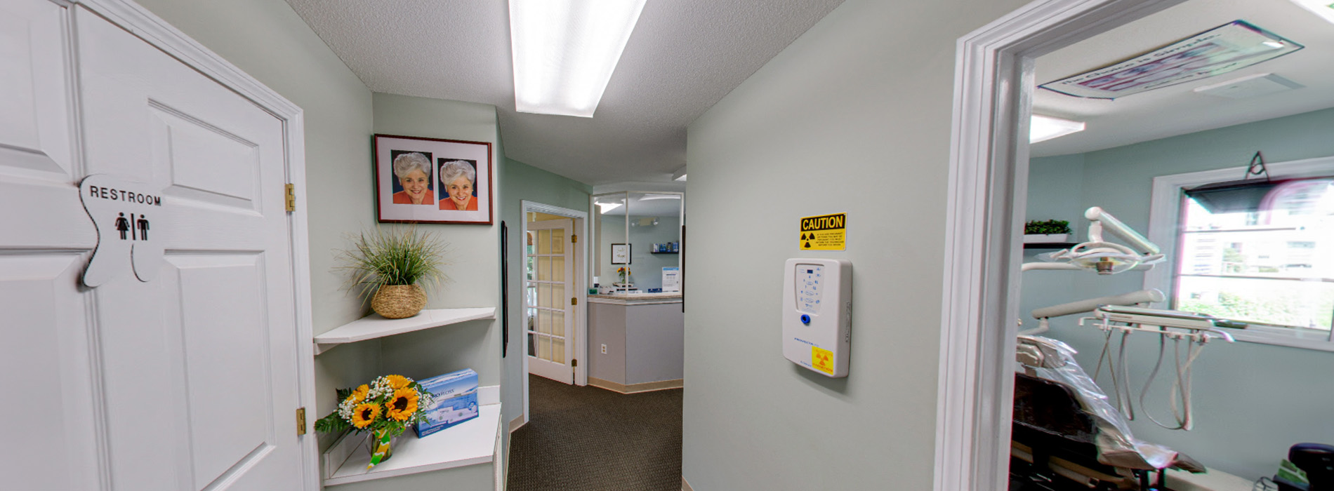The image shows an interior space with a room that appears to be a dental office, featuring dental equipment and a reception area, with a panoramic view of a waiting area and hallway.