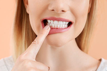 A woman with her finger on her lip, showing a toothy smile, against a plain background.